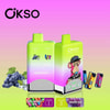 Zwei Okso-Vape-Geräte mit doppeltem Geschmack in Grün und Lila mit den Geschmacksrichtungen Red Energy Ice und Grape Ice, mit einem Cartoon-Affen mit einer Kappe, umgeben von Bildern von Trauben, Energydrink-Dosen und Geschmacksetiketten auf einem rosa und grünen Hintergrund mit Farbverlauf.