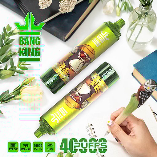 Green And Yellow Bang King Disposable Vape Devices Featuring An Illustrated Gorilla With A Helmet, Placed On A White Surface With Flowers, Books, And A Hand Writing With An Owl Pen Nearby; Promotional Text Highlights '40,000 Puffs' And Device Specifications.