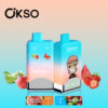 Two Okso Double Flavor Vape Devices With A Blue And Gradient Design, Featuring Flavors Strawberry Watermelon And Two Apple, And A Cartoon Monkey Illustration With Images Of Apples, Strawberries, And Watermelon In The Background.