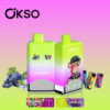 Two Okso Double Flavor Vape Devices In Green And Purple Gradient With The Flavors Red Energy Ice And Grape Ice, Featuring A Cartoon Monkey With A Cap, Surrounded By Images Of Grapes, Energy Drink Cans, And Flavor Labels On A Pink And Green Gradient Background.