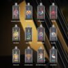 Twelve Vape Devices With Illustrated Animal Designs, Each Representing A Different Flavor Such As Strawberry Watermelon, Blue Razz Ice, Triple Berry Ice, Peach Ice, Peach Mango, Double Apple, Strawberry Kiwi, Aloe Grape, Tropical Fruit, Strawberry Banana, Kiwi Passion Fruit Guava, And Black Dragon Ice, Displayed Against A Dark And Gold Geometric Background.