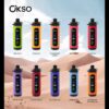 Tien kleurrijke OKSO vape -apparaten worden weergegeven in twee rijen, elk gelabeld met een andere smaaknaam zoals twee appel, perzikijs en blauw razzijs, tegen een achtergrond van een woestijnlandschap.